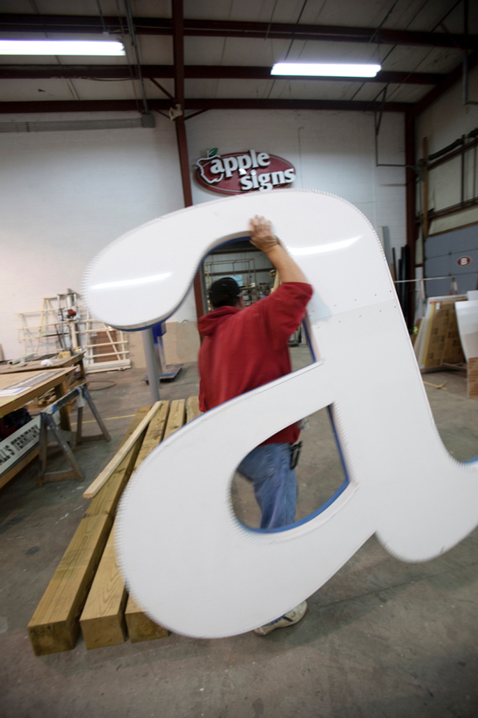 man walking through sign facility carrying large letter A